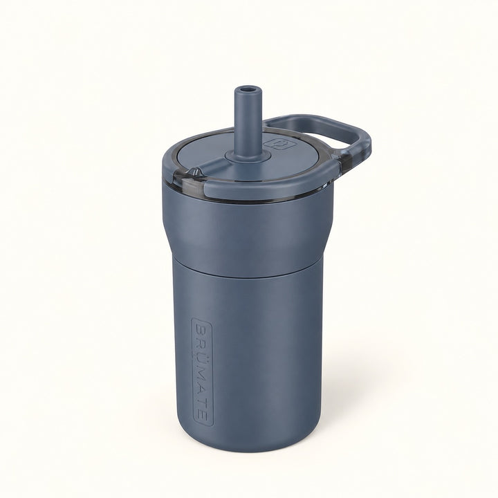 BrüMate Leap 12oz Kids Straw Tumbler in Nightfall Blue featuring a compact insulated body, matching protective silicone sleeve, flip-style lid with upright drinking straw, and small carrying handle. Displayed against a clean white studio background.