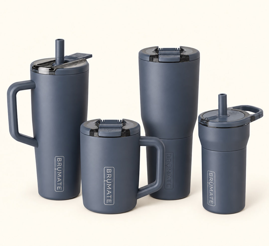 Four matte slate blue insulated tumblers with lids from Brumate, displayed in a clean studio arrangement on a light cream background.