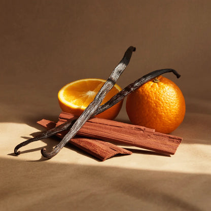 Vanilla beans, cinnamon sticks, and oranges on a beige background