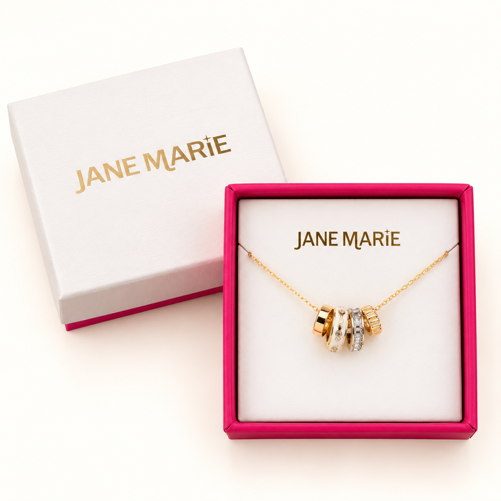Jane Marie gold crystal and white rondelle necklace displayed in an open pink jewelry box beside its white Jane Marie gift box lid on a cream background.