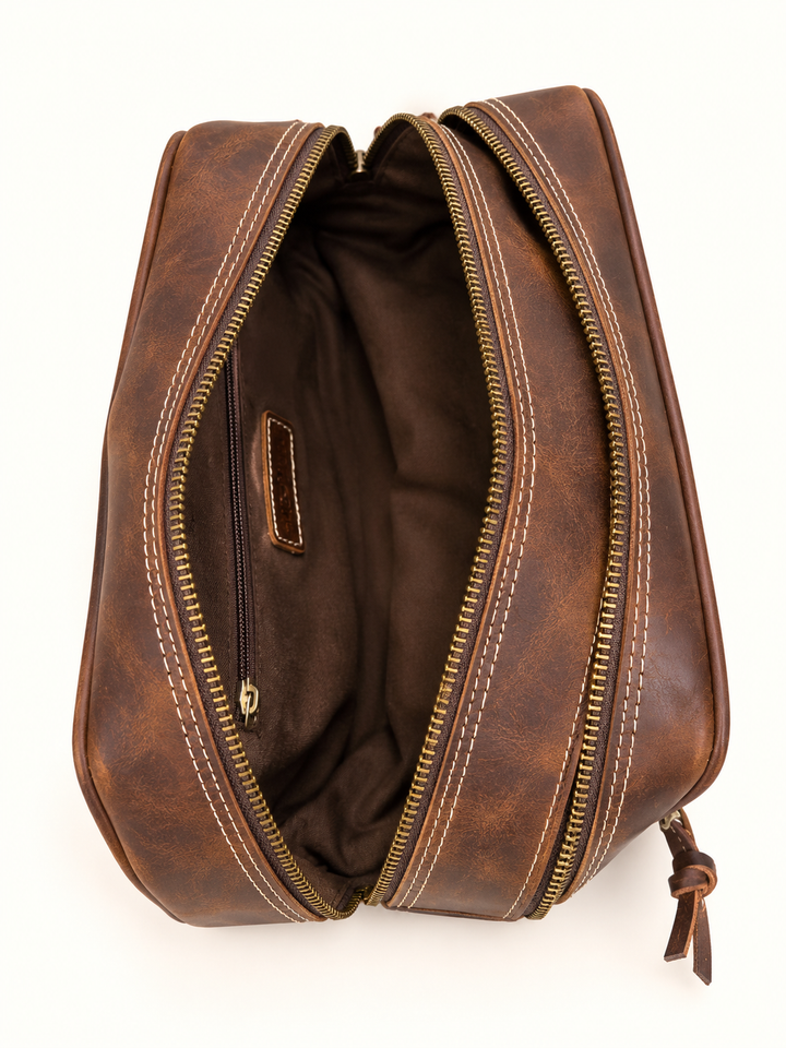 Overhead interior view of the Dusty Dopp Kit brown leather toiletry bag showing the spacious fabric-lined compartment, interior zippered pocket, and open brass zipper on a cream background.