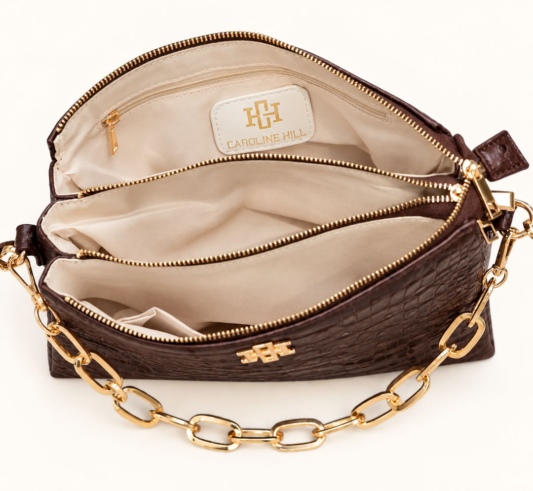 Interior view of the Caroline Hill Ariana chocolate croc crossbody bag featuring multiple compartments, zippered sections, cream lining, and gold hardware.

