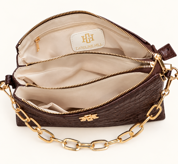 Interior view of the Caroline Hill Ariana chocolate croc crossbody bag featuring multiple compartments, zippered sections, cream lining, and gold hardware.
