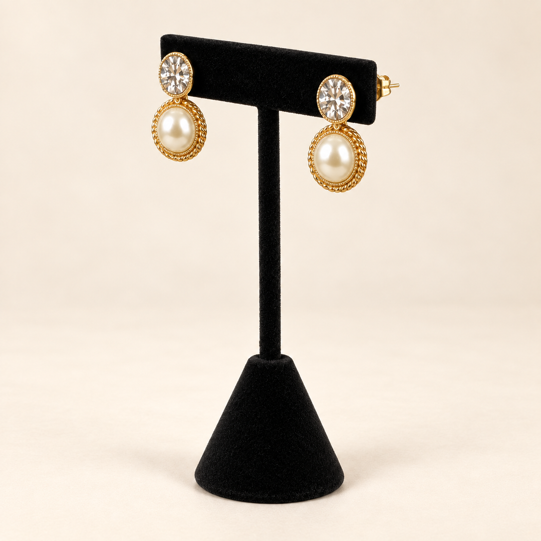 Angled view of gold-tone round pearl textured drop earrings with clear crystal studs and ivory pearl drops on a black velvet stand.