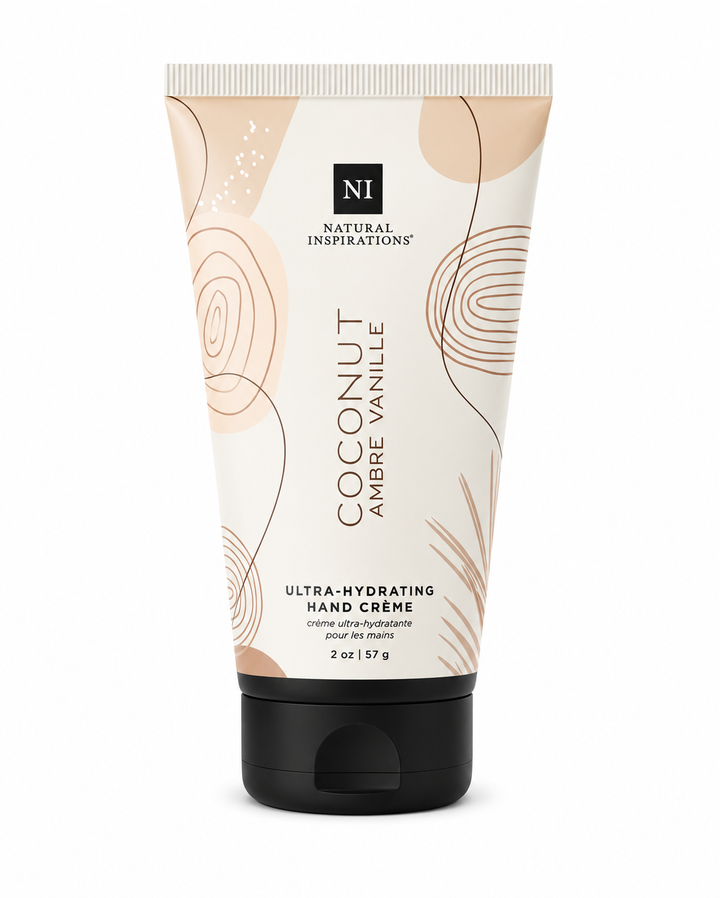 Natural Inspirations Coconut Ambre Vanille Ultra-Hydrating Hand Crème (2 oz / 57 g) in a cream-colored squeeze tube with warm beige botanical accents and a black flip-top cap, photographed on a clean white studio background.