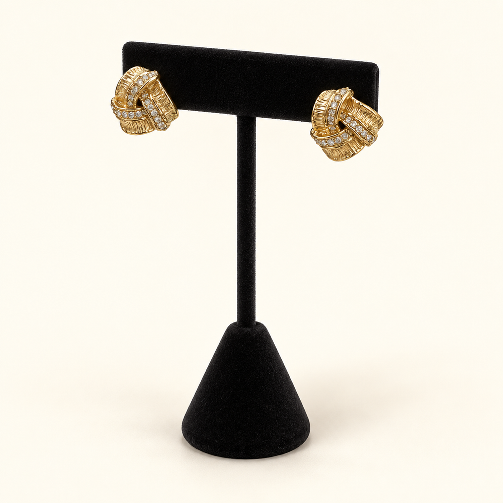 Angled view of gold-tone pavé love knot earrings showing the textured intertwined design and sparkling stone accents.