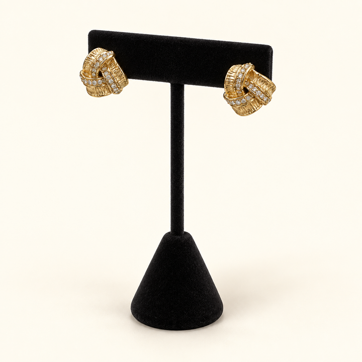 Angled view of gold-tone pavé love knot earrings showing the textured intertwined design and sparkling stone accents.