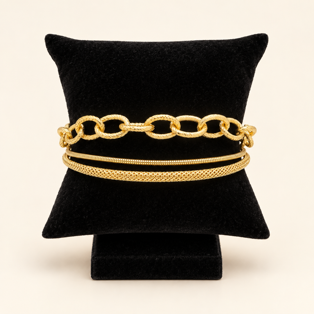 Front view of the Golden Layers gold three-row bracelet featuring oval links, a snake chain and a textured woven chain on a black velvet pillow.