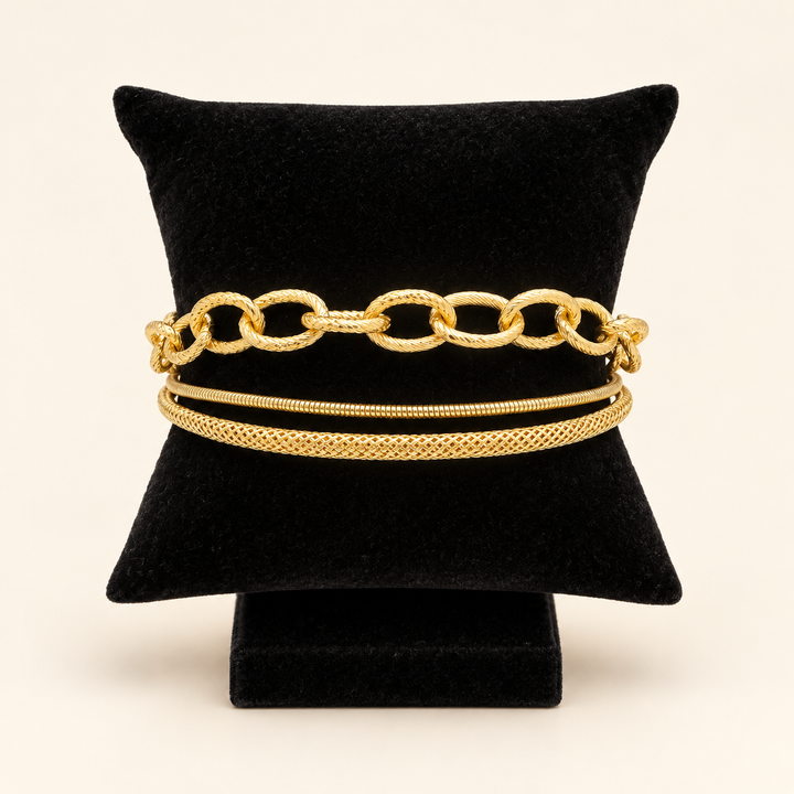 Front view of the Golden Layers gold three-row bracelet featuring oval links, a snake chain and a textured woven chain on a black velvet pillow.