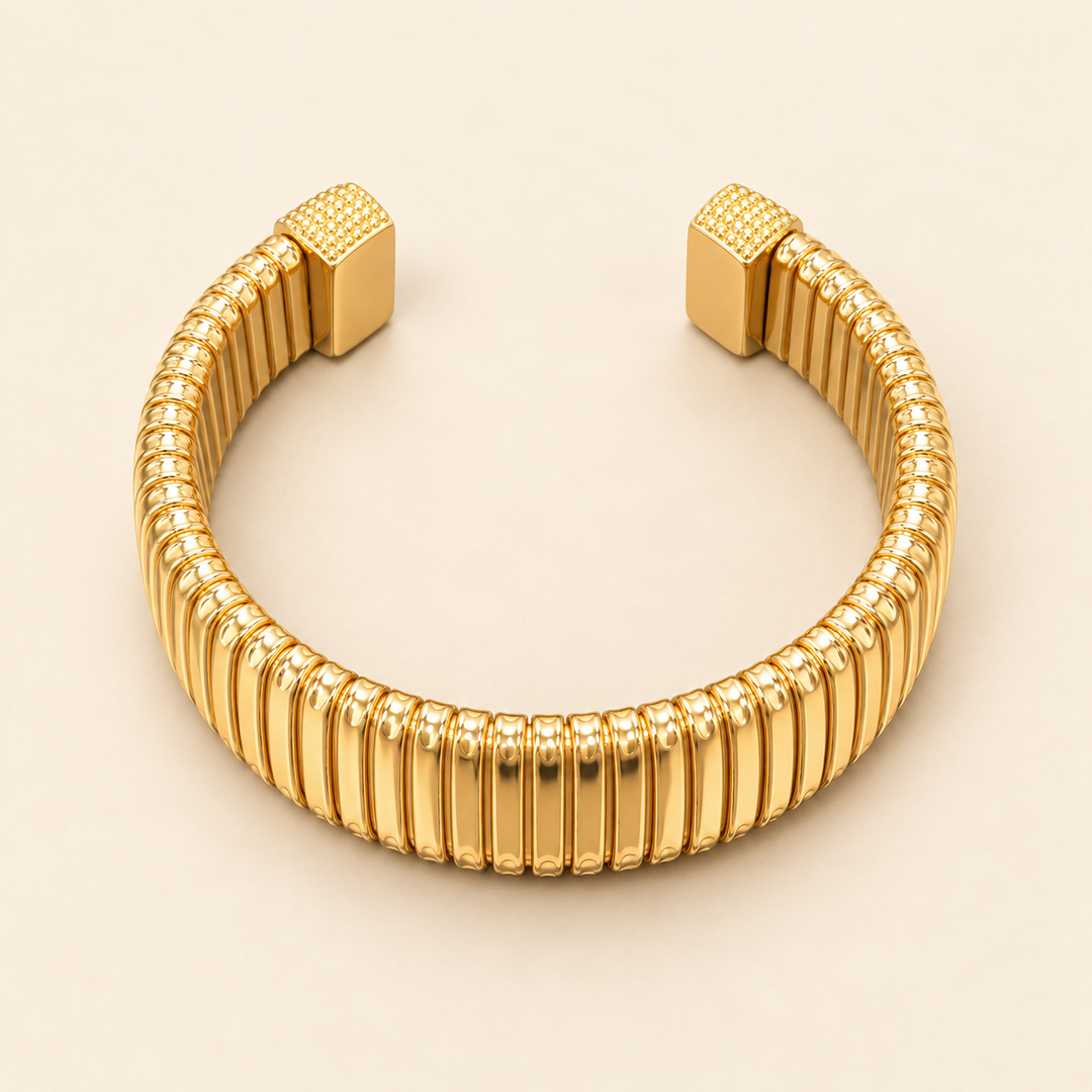 Open gold Omega cuff bracelet with vertical ribbed detailing and textured square end caps flat-laid on a cream background.