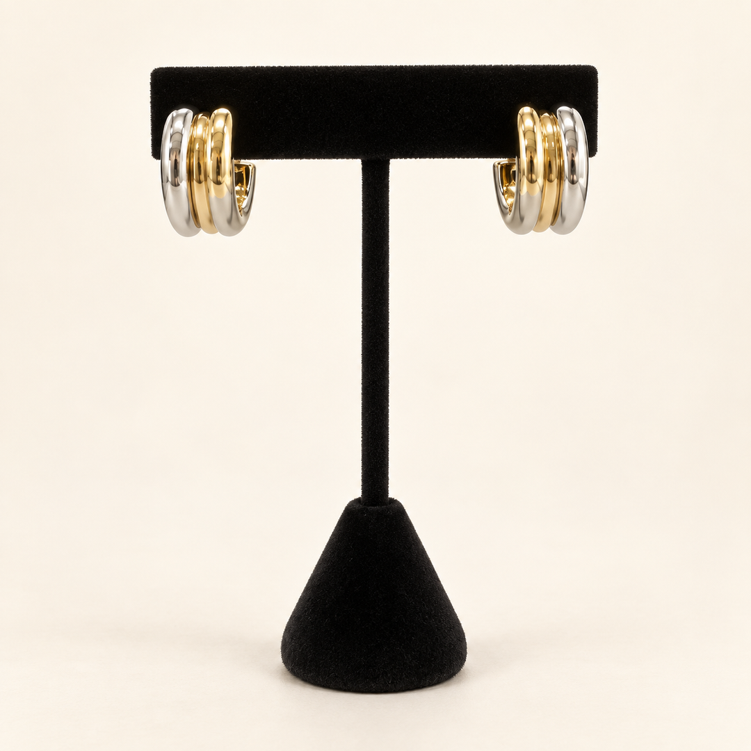 Two-tone layered hoop earrings with three polished gold and silver bands displayed on a black velvet earring stand against a cream background.
