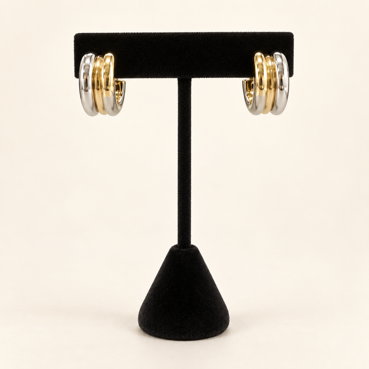 Two-tone layered hoop earrings with three polished gold and silver bands displayed on a black velvet earring stand against a cream background.