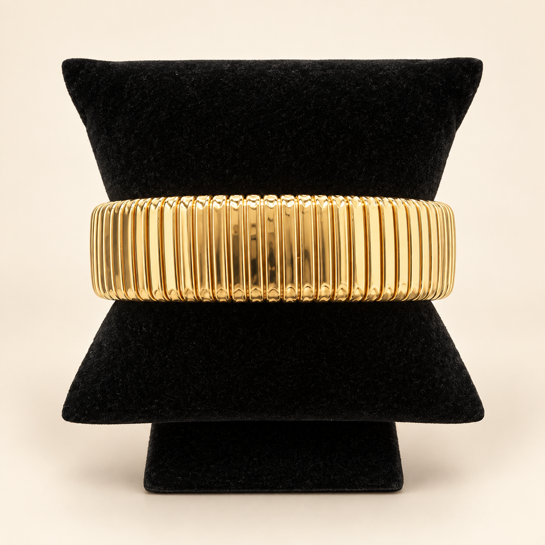 Gold Omega cuff bracelet with a wide ribbed design displayed on a black velvet bracelet stand against a cream background.