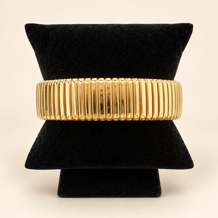 Gold Omega cuff bracelet with a wide ribbed design displayed on a black velvet bracelet stand against a cream background.