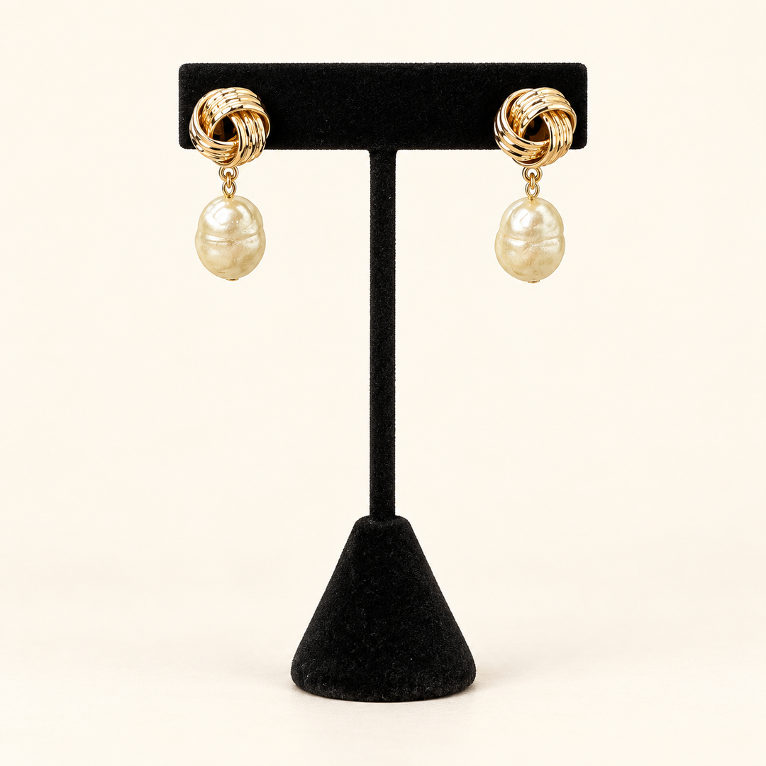 Front view of gold knot earrings with irregular ivory baroque pearl drops displayed on a black velvet stand.