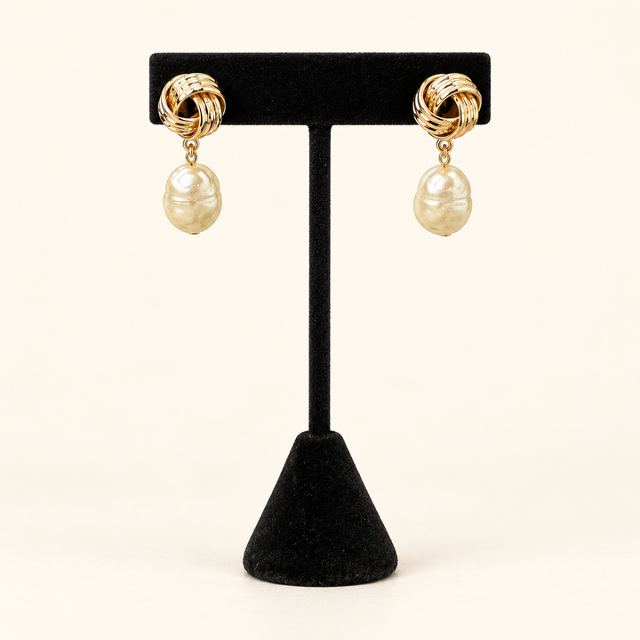 Front view of gold knot earrings with irregular ivory baroque pearl drops displayed on a black velvet stand.