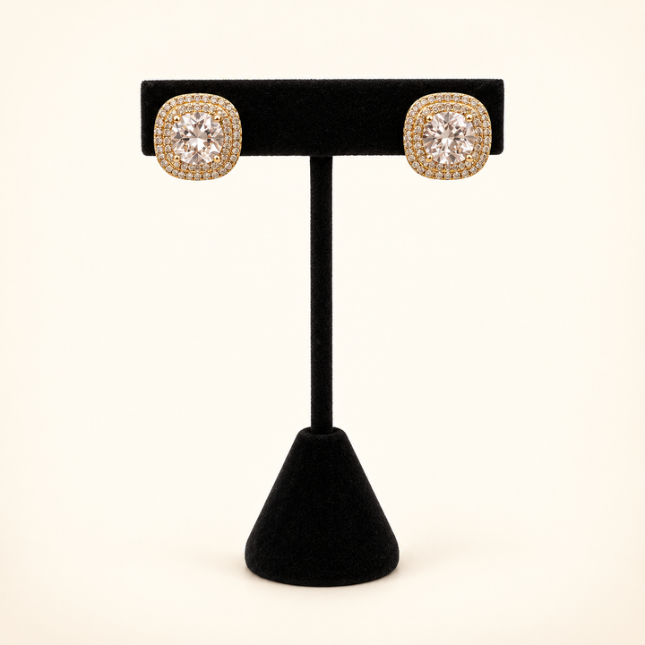 Gold square CZ halo stud earrings with large clear center stones displayed on a black velvet stand against a cream background.