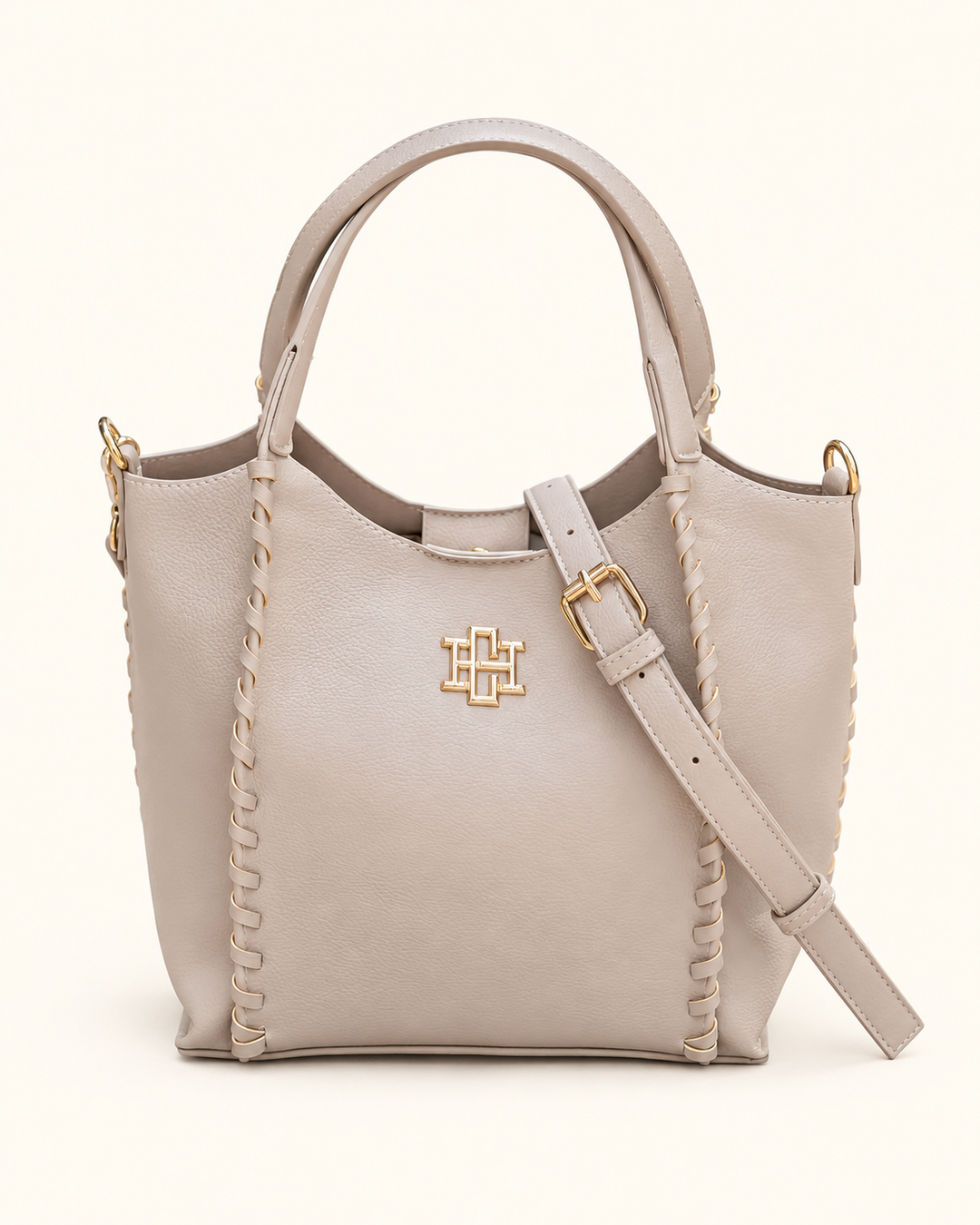 Front view of the Caroline Hill Allison Tote in Stone with whipstitch detailing, gold logo hardware, top handles, and an adjustable crossbody strap.