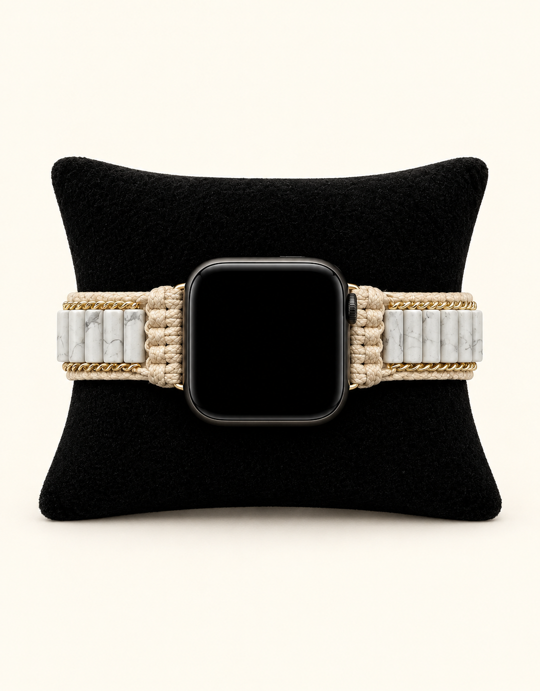 A woven watch band in beige and white with gold-toned chain accents, shown on a black watch with a black screen, displayed on a black velvet cushion against a light cream background.