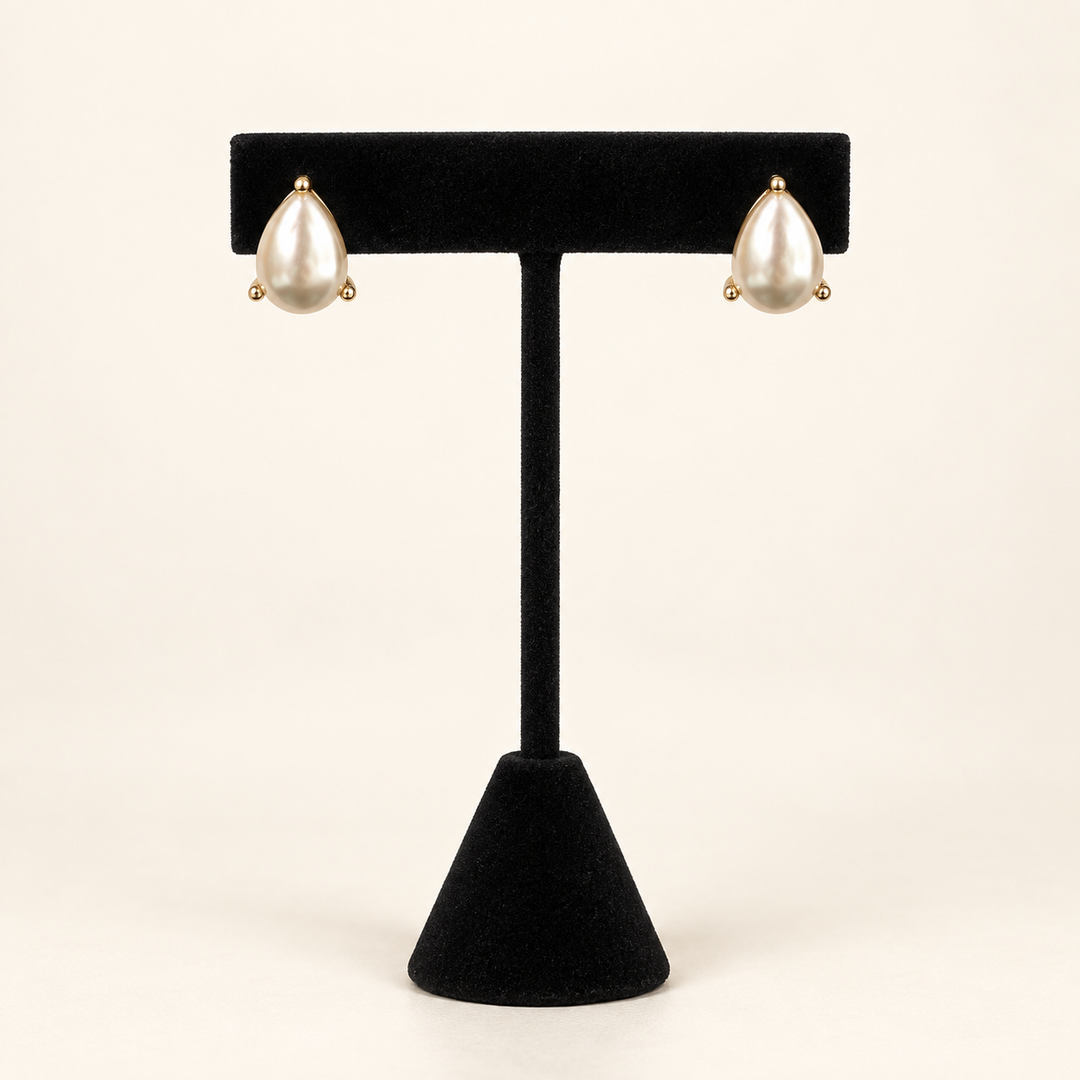 Front view of Lustrous Teardrop Pearl Earrings in gold-tone settings displayed on a black velvet jewelry stand.