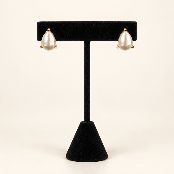 Front view of Lustrous Teardrop Pearl Earrings in gold-tone settings displayed on a black velvet jewelry stand.