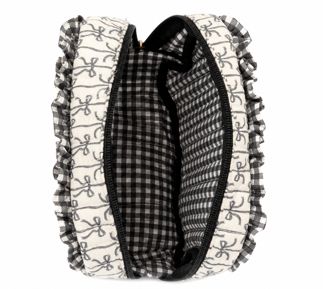 Open Simply Southern Black Bow Quilted Cosmo Bag featuring a black bow print exterior, ruffle trim, black zipper, and spacious black-and-white gingham lined interior with organizational pockets on a clean white studio background.