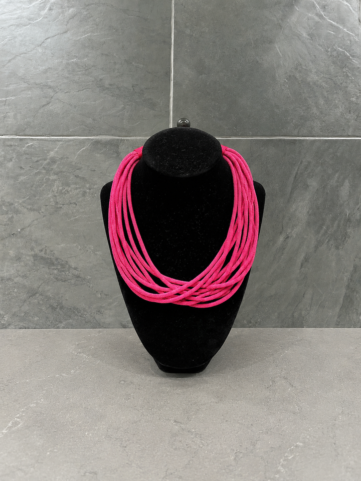 Hot pink multi-strand cord statement necklace showcased on a black velvet jewelry bust against a gray stone background.