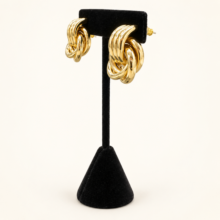 Angled view of gold layered knot earrings showing the interlocking loops and dimensional design on a black velvet stand.