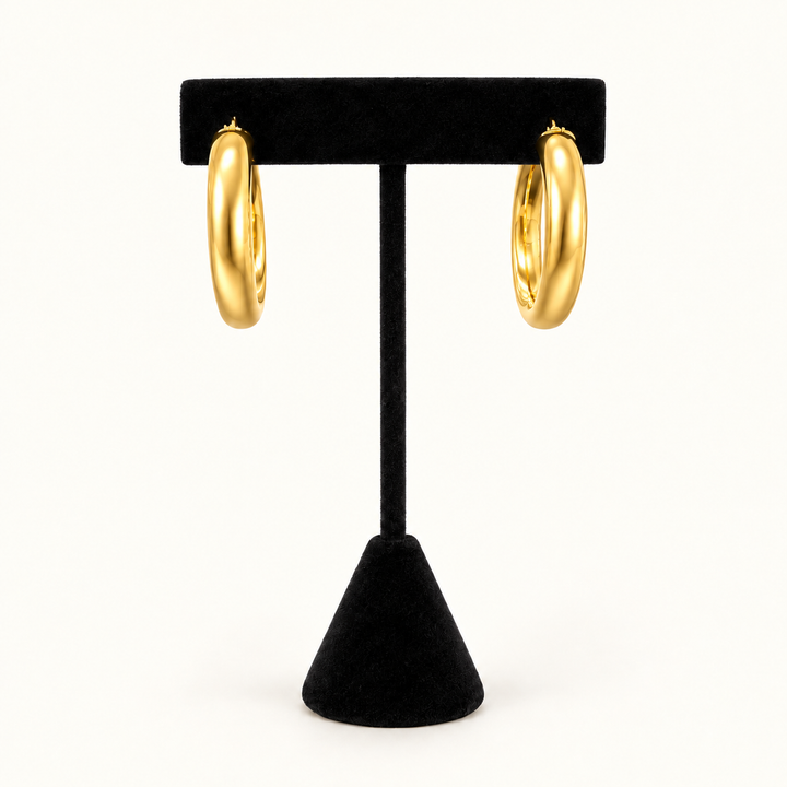 Front view of polished gold triple-ridge hoop earrings displayed on a black velvet stand against a cream background.