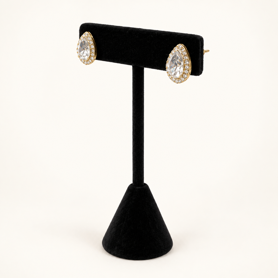 Angled view of gold teardrop halo stud earrings with clear faceted stones displayed on a black velvet stand.