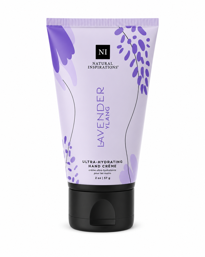 Natural Inspirations Lavender Ylang Ultra-Hydrating Hand Crème (2 oz / 57 g) in a soft lavender squeeze tube with purple botanical artwork and a black flip-top cap, isolated on a white studio background.