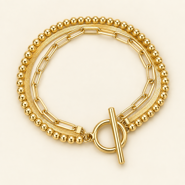 Close-up flat lay of the Linked Luxe bracelet showing its gold-tone toggle closure, ball strand, snake chain and elongated paperclip links.