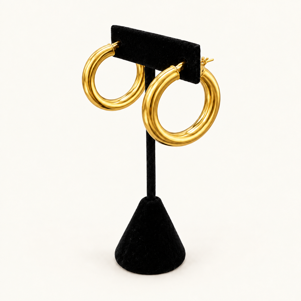 Angled view of polished gold triple-ridge hoop earrings showing the rounded shape and dimensional design on a black velvet stand.