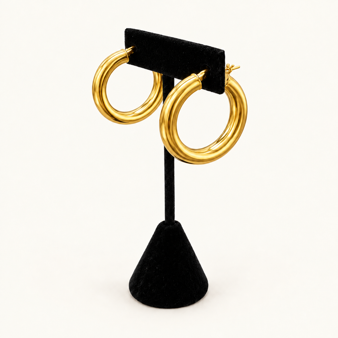 Angled view of polished gold triple-ridge hoop earrings showing the rounded shape and dimensional design on a black velvet stand.