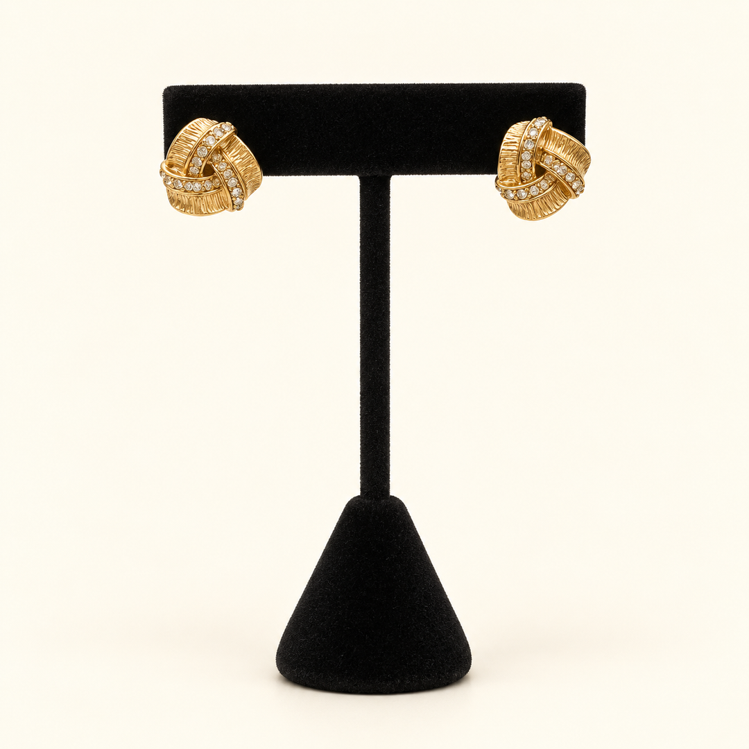 Front view of Forever Entwined gold-tone pavé love knot earrings displayed on a black velvet jewelry stand.
