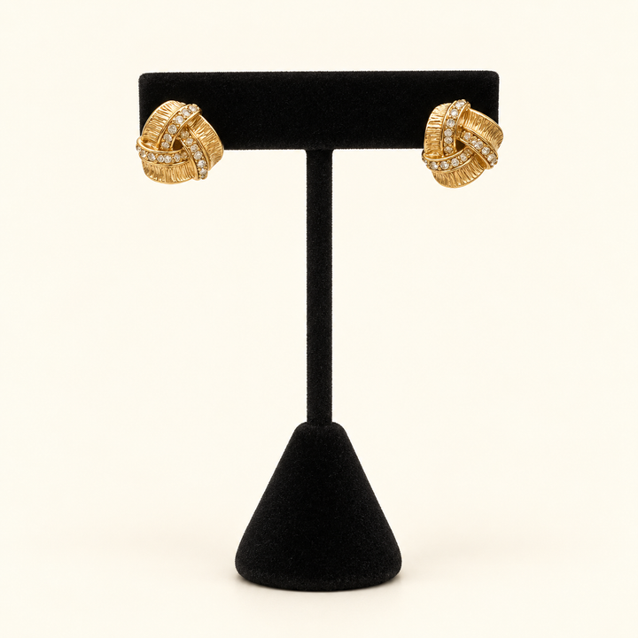 Front view of Forever Entwined gold-tone pavé love knot earrings displayed on a black velvet jewelry stand.
