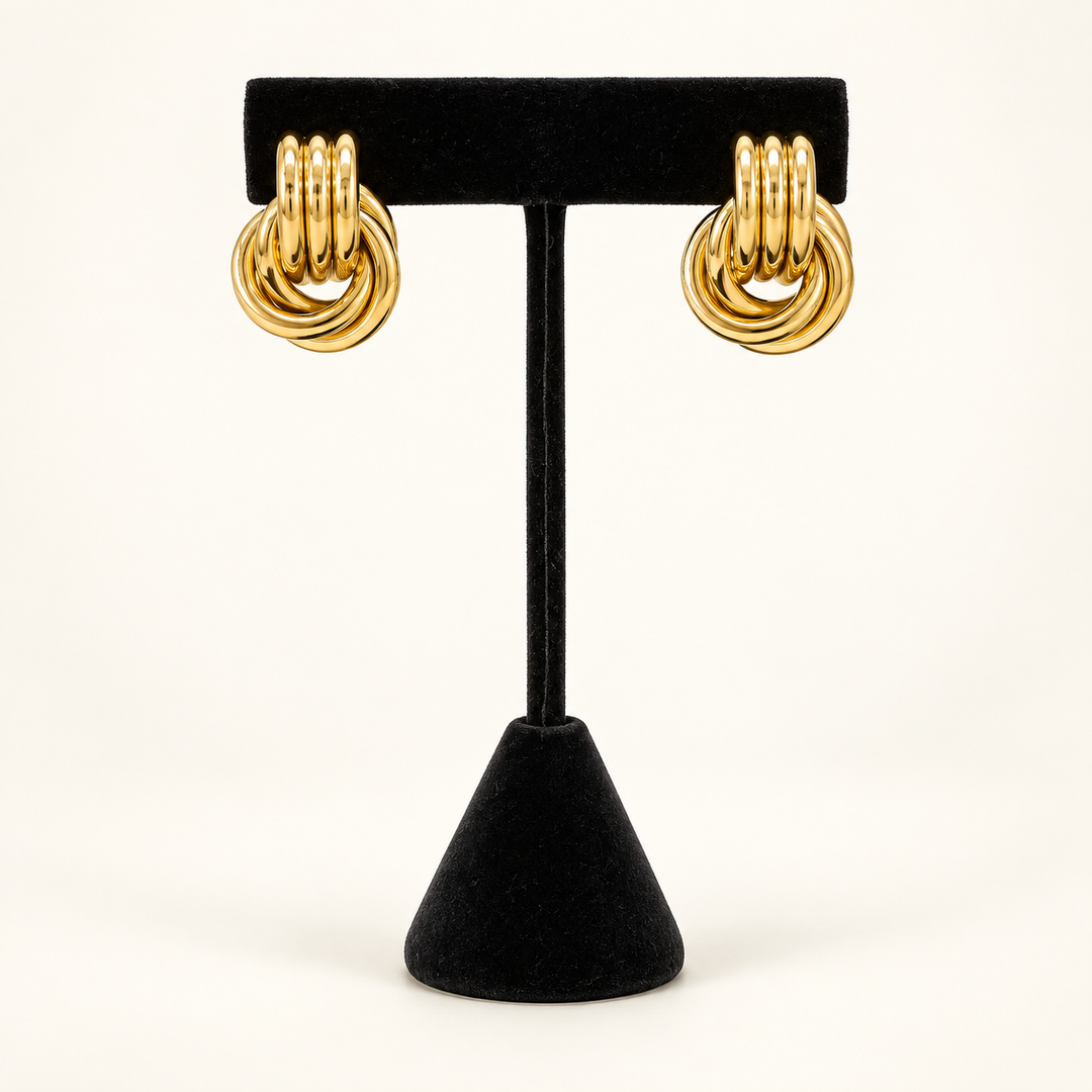 Front view of polished gold layered knot drop earrings displayed on a black velvet stand.