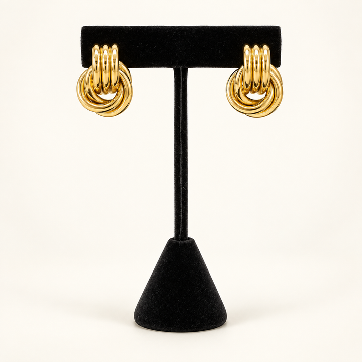 Front view of polished gold layered knot drop earrings displayed on a black velvet stand.