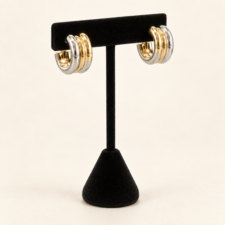 Angled view of two-tone layered hoop earrings featuring three polished gold and silver bands on a black velvet stand against a cream background.