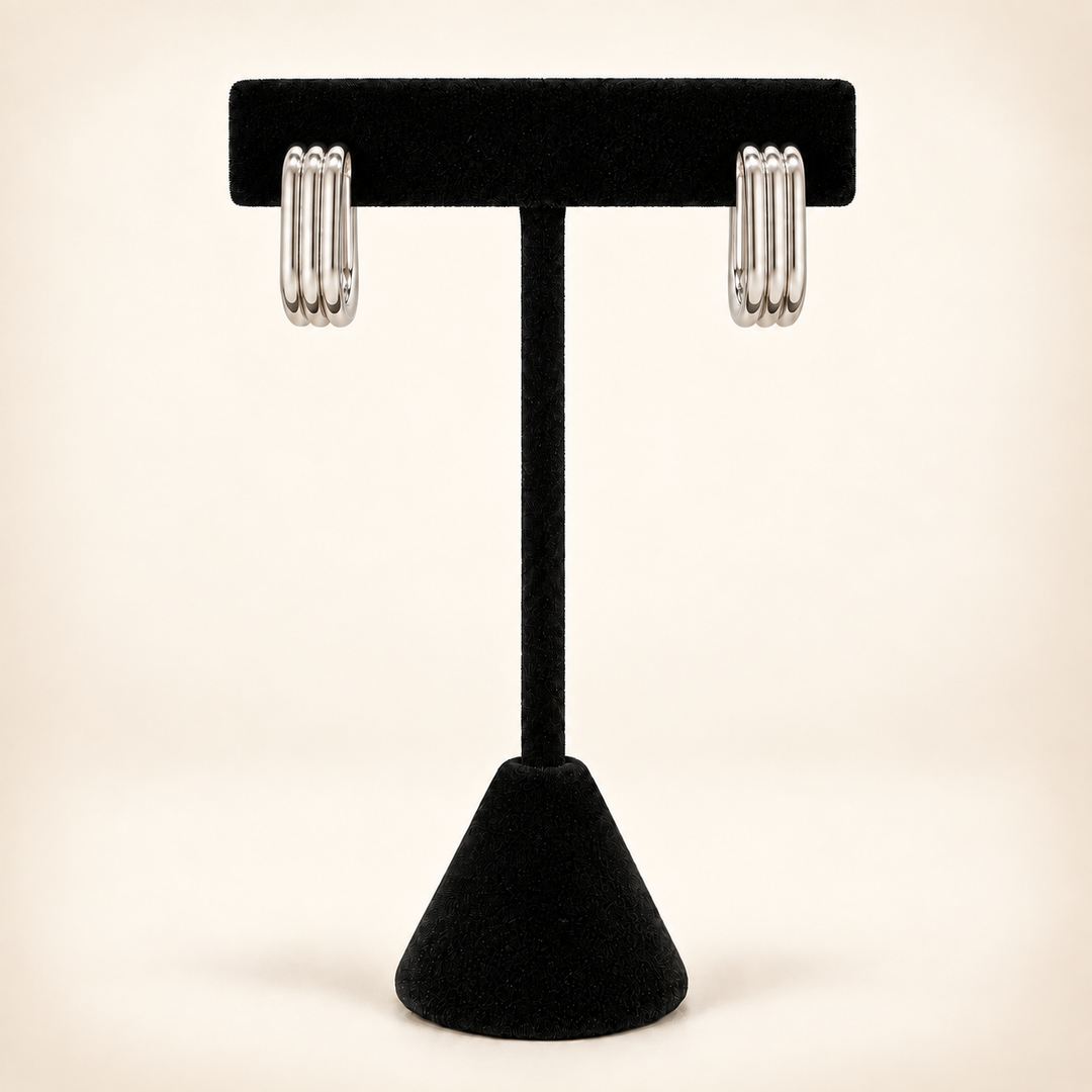 Front view of polished silver four-row rectangular hoop earrings displayed on a black velvet stand against a cream background.