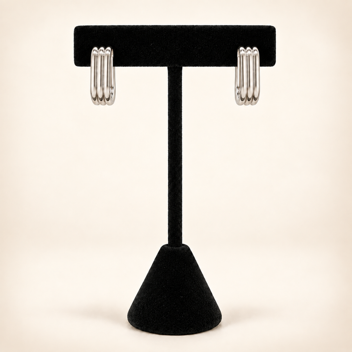 Front view of polished silver four-row rectangular hoop earrings displayed on a black velvet stand against a cream background.