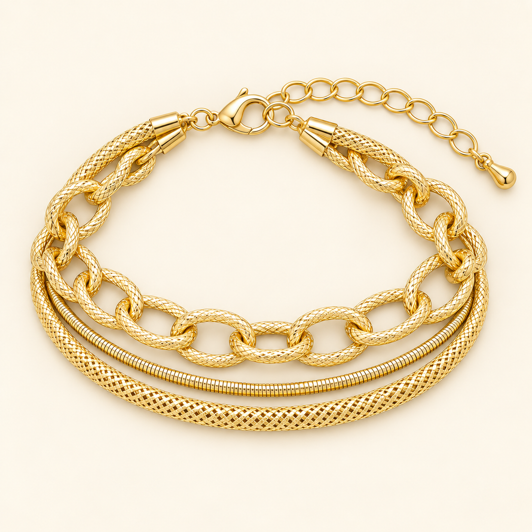 Flat lay of the Golden Layers gold three-row bracelet featuring textured oval links, a smooth snake chain, a woven chain, lobster clasp and extender.