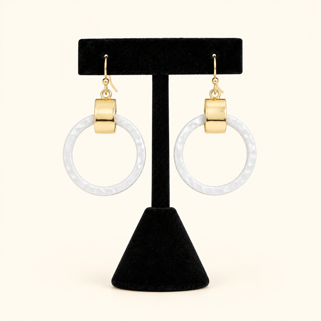 2-inch white circular drop earrings with gold-tone rectangular accents and fishhook closures displayed on a black velvet jewelry stand against a cream background.