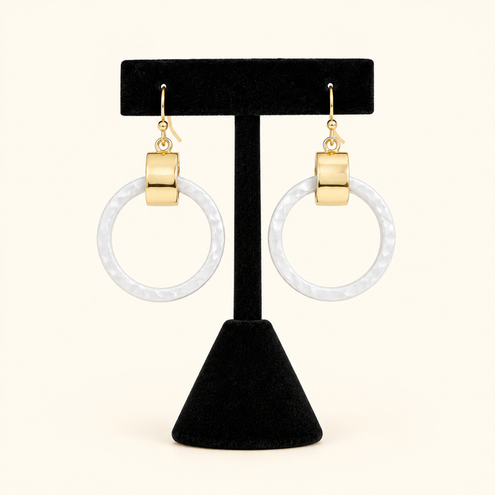 2-inch white circular drop earrings with gold-tone rectangular accents and fishhook closures displayed on a black velvet jewelry stand against a cream background.