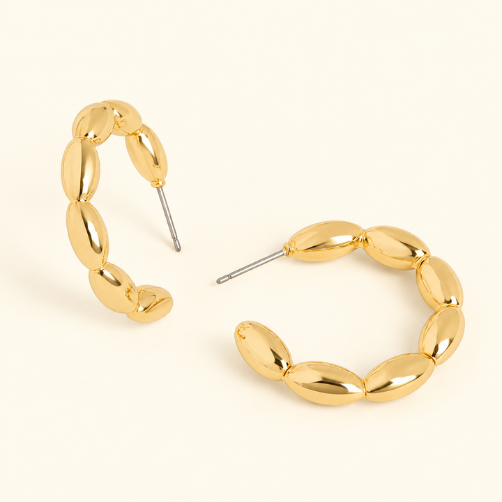 Gold-tone 1-inch hoop earrings featuring polished oval bead segments, an open hoop design, and post closures on a cream background.