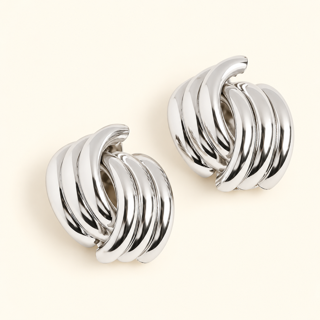 Silver-tone chunky knot hoop earrings featuring polished, layered curved bands in a 0.5-inch design on a cream background.