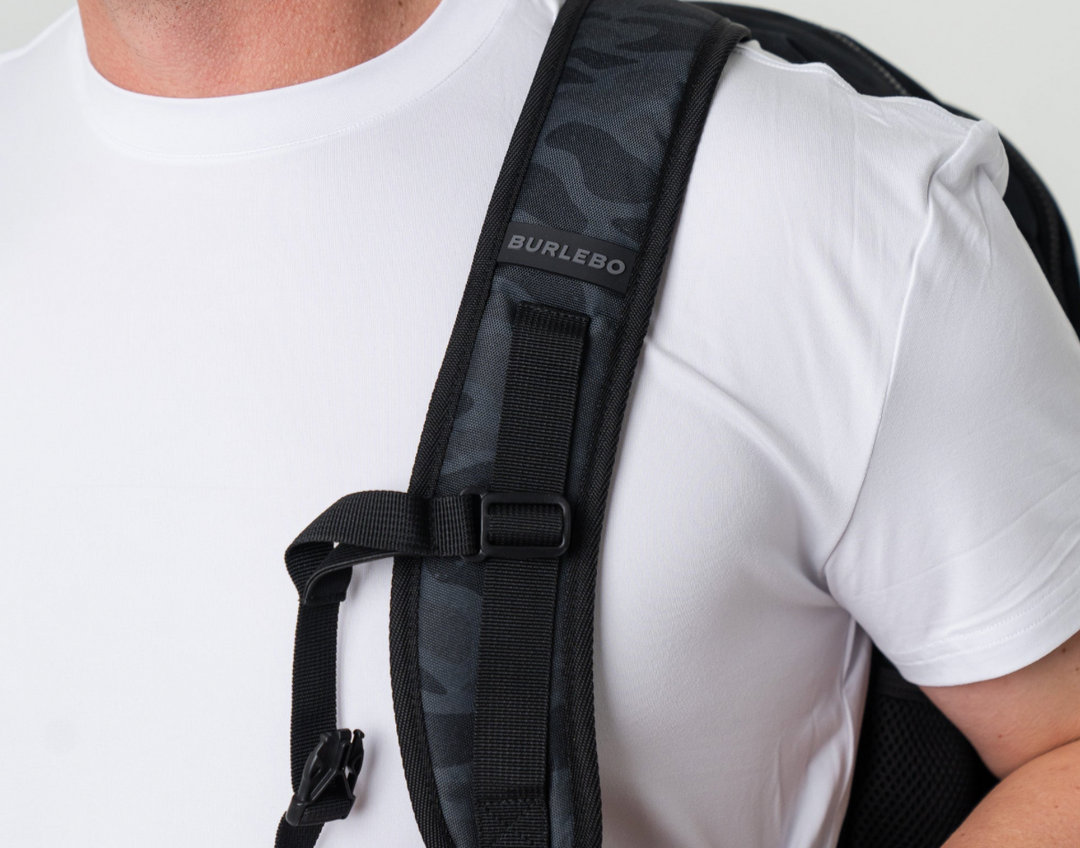 Person wearing the Burlebo Black Camo backpack over one shoulder, showcasing the adjustable padded shoulder strap and comfortable everyday fit.
