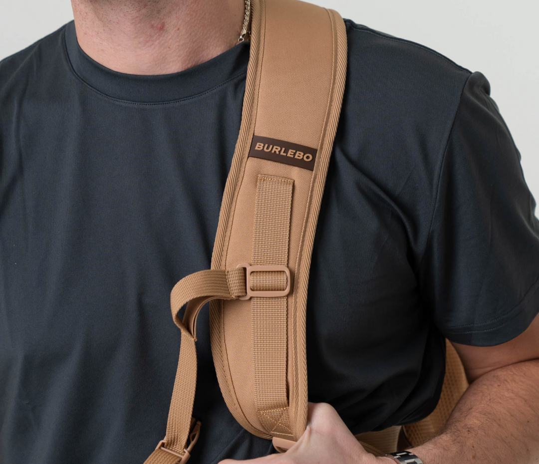 Person wearing the Burlebo Coyote Tan backpack over one shoulder, showcasing the adjustable padded shoulder strap and comfortable everyday fit.