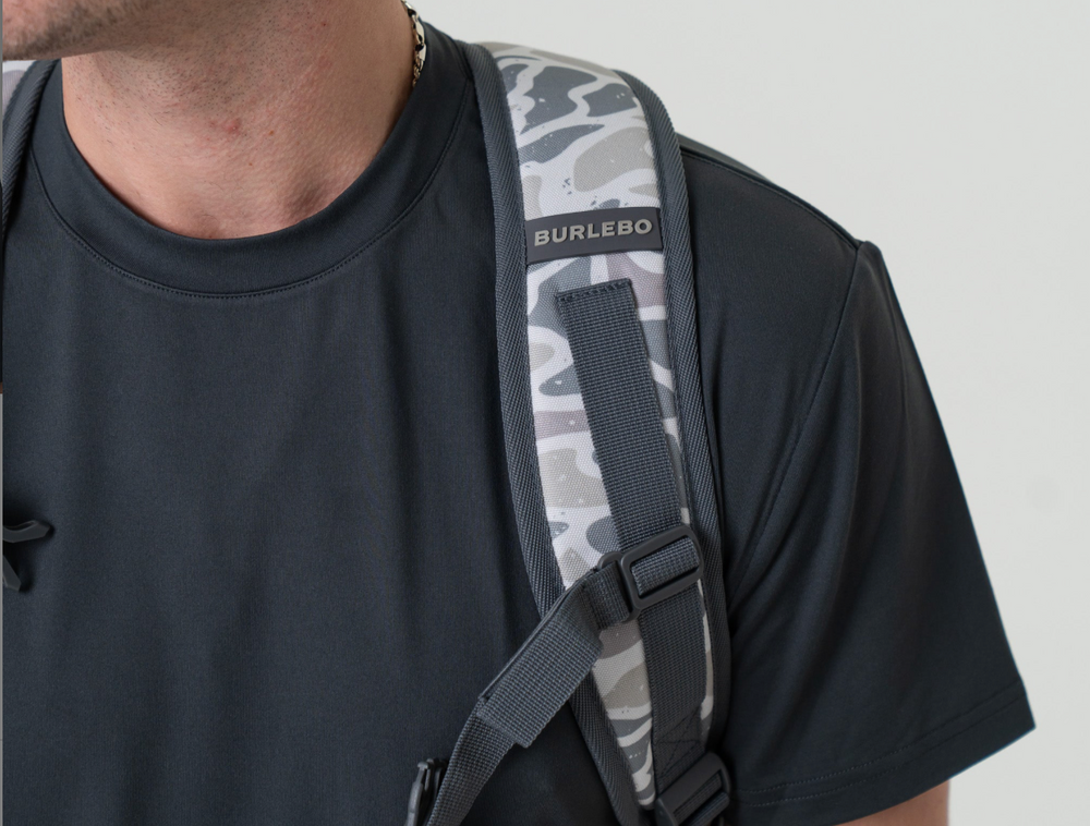Person wearing the Burlebo White Camo backpack over one shoulder, showcasing the adjustable padded shoulder strap and comfortable everyday fit.