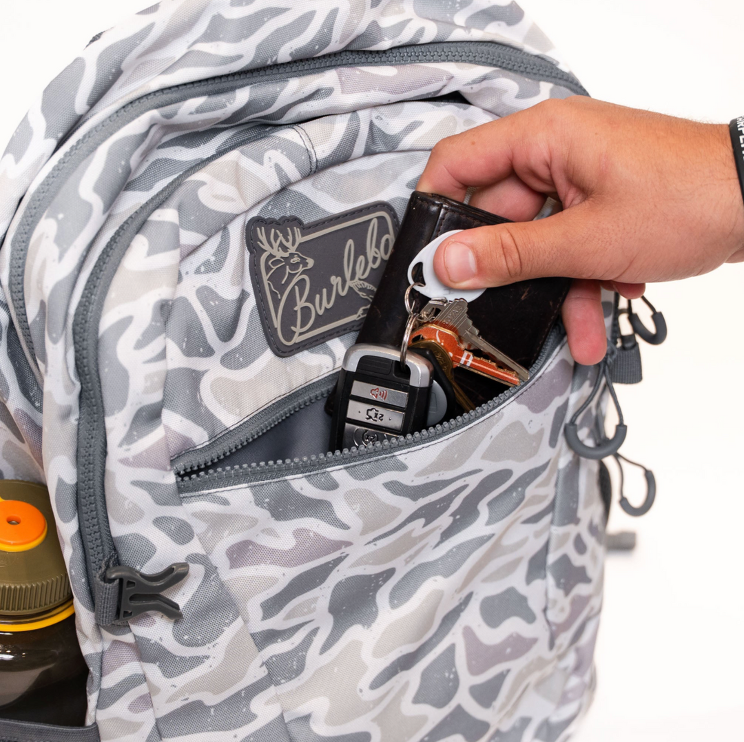 Close-up of the Burlebo White Camo backpack front zipper pocket holding everyday accessories for quick and convenient access.